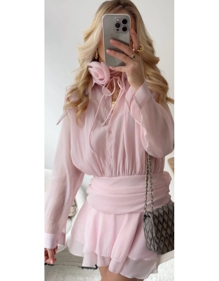 Ρομαντικό φόρεμα σε απαλό ροζ, με δέσιμο στο λαιμό και εντυπωσιακό λουλούδι. Αέρινη γραμμή, κουμπιά μπροστά και ζώνη στη μέση που αναδεικνύει τη σιλουέτα.