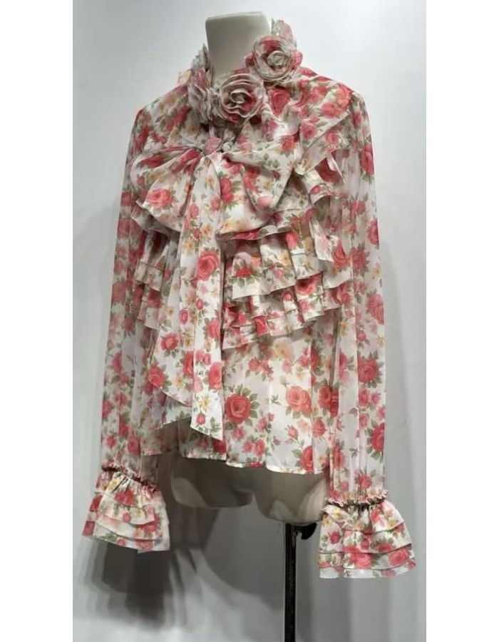 Αέρινη μπλούζα με ρομαντικό floral print σε αποχρώσεις ροζ, διακοσμημένη με εντυπωσιακά βολάν και φιόγκο μπροστά. Διαθέτει ιδιαίτερες λεπτομέρειες στον γιακά με τριαντάφυλλα και μακριά μανίκια με βολάν στο τελείωμα